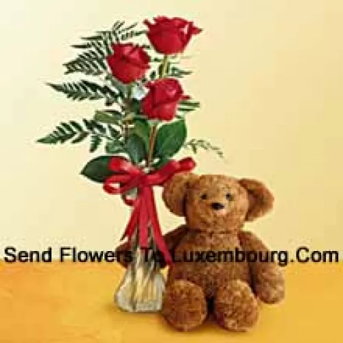 玻璃花瓶里有3朵红玫瑰和一些蕨类植物，外加一个可爱的12英寸高的泰迪熊