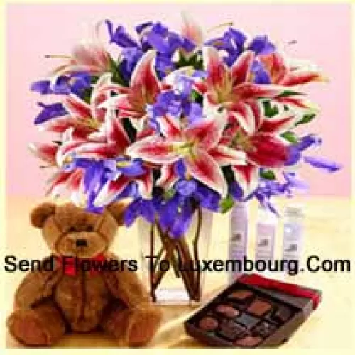 Розовые лилии и разноцветные фиолетовые цветы красиво уложены в стеклянной вазе, милый 12-дюймовый коричневый плюшевый медведь и импортированный шоколад